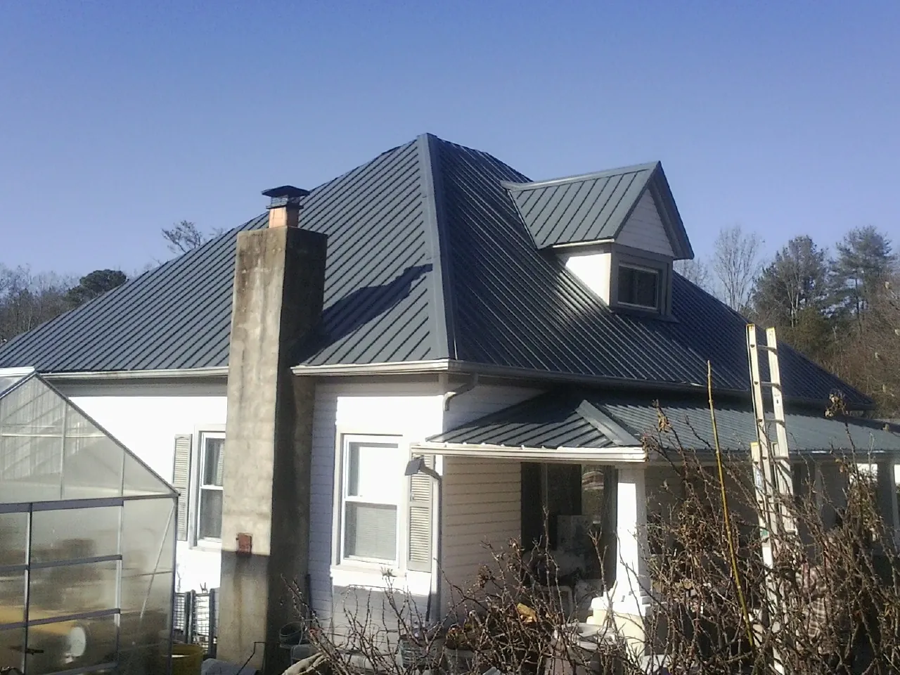 Dark blue standing seam metal roof on a white farmhouse with dormer — Slate & Tile Roof Repair by Roofing Brothers in Melvin Village