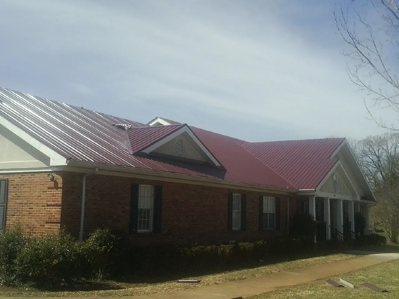 Red metal roof with gabled entries on a long brick building, from a Hail Damage Roof Repair job in Melvin Village