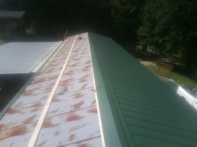 Old rusted panels beside newly installed green metal roofing — Wind Damage Roof Repair by Roofing Brothers in Melvin Village
