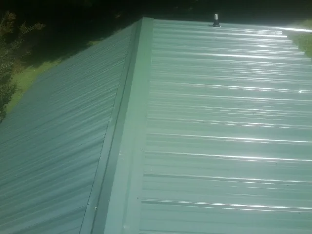 New green metal panels meeting at the ridge of a roof — Flat Roof Repair work by our crew in Melvin Village