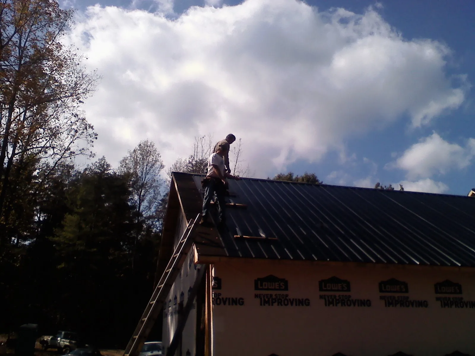 Roofer fastening dark metal panels high against a cloudy sky, from a Roof Inspection job in Melvin Village