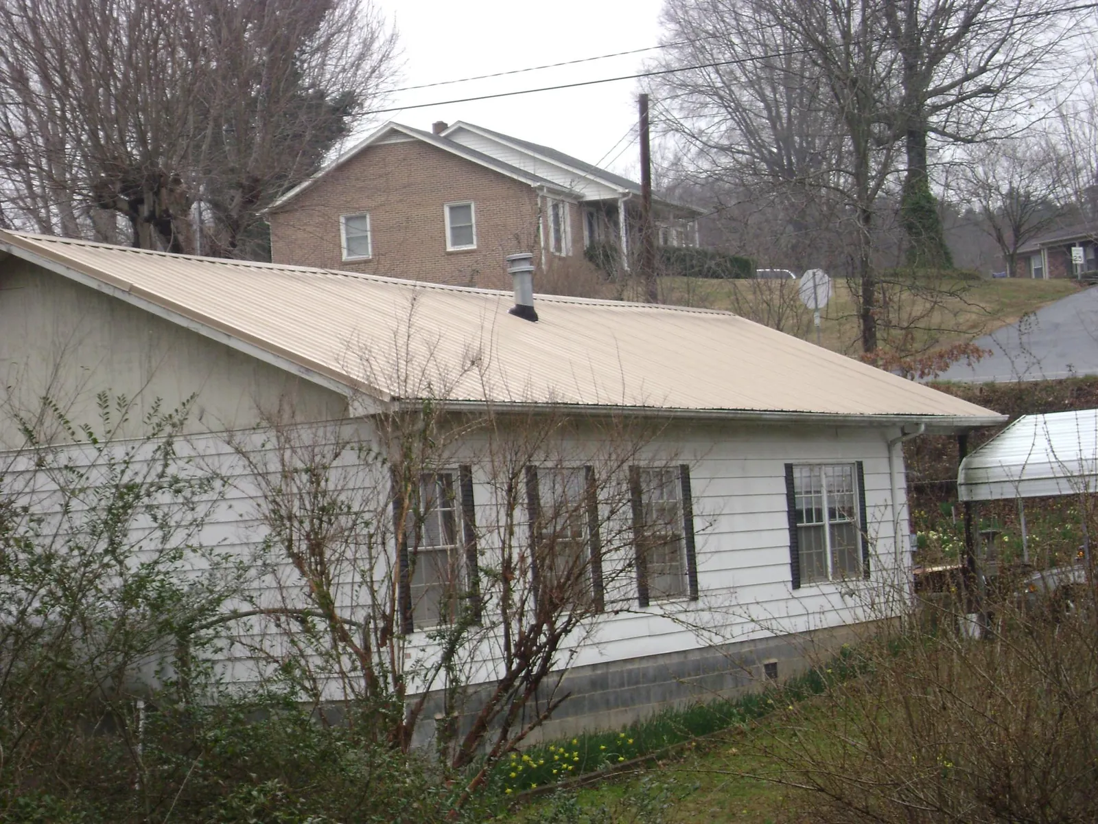 Tan metal roof on a white sided house set into a hillside — Commercial Roofing by Roofing Brothers in Melvin Village