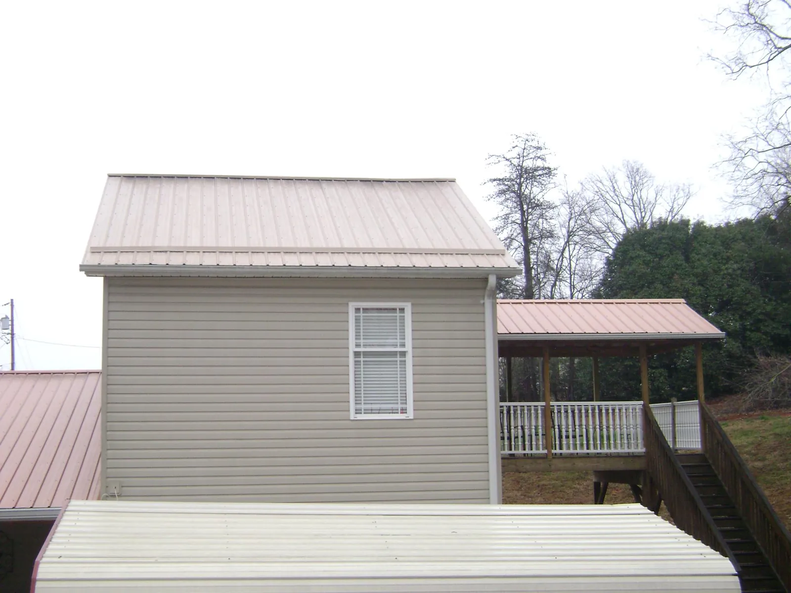 Tan metal roofs on a two story addition and attached porch, from a Roof Replacement job in Melvin Village